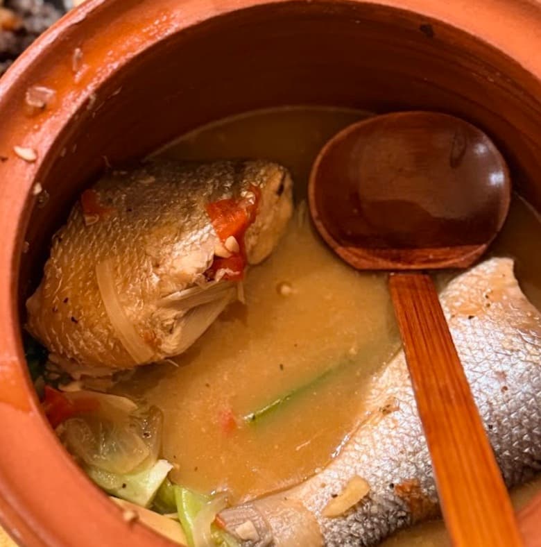 Sinigang na bangus in a clay pot — milkfish in sour broth, wooden ladle resting in it.