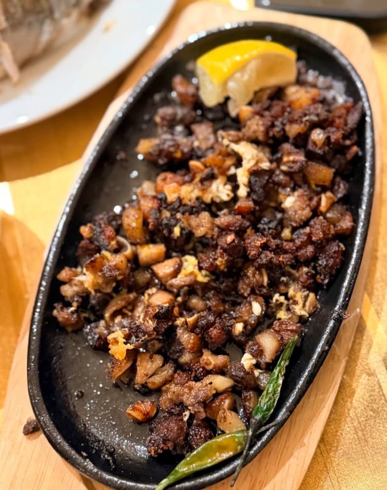 Sisig on a sizzling cast-iron plate, with citrus and green chillies.